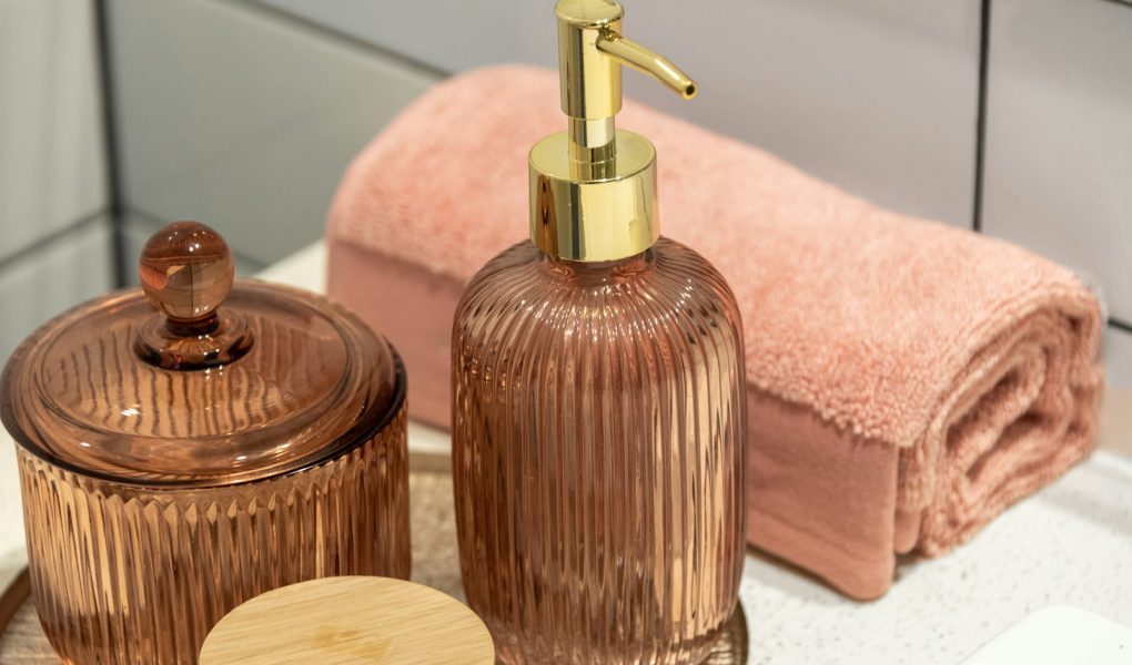 A soap dispenser and a rolled pink towel on a bathroom counter