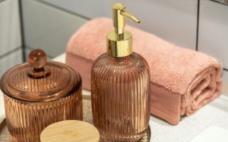 A soap dispenser and a rolled pink towel on a bathroom counter