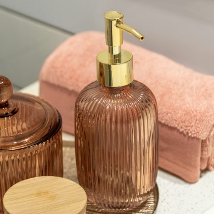 A soap dispenser and a rolled pink towel on a bathroom counter