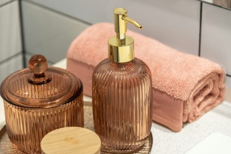 A soap dispenser and a rolled pink towel on a bathroom counter