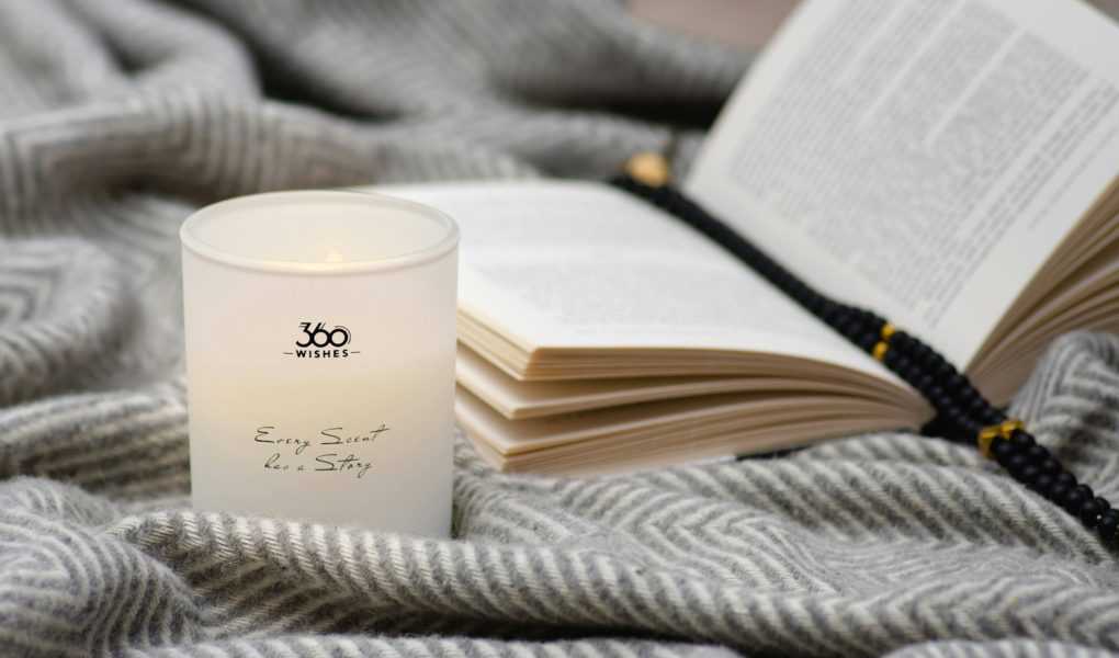 A candle and an open book on a soft gray blanket