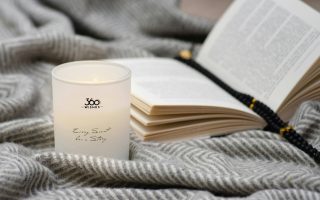 A candle and an open book on a soft gray blanket