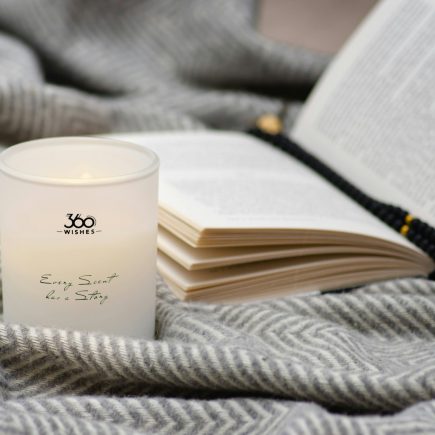 A candle and an open book on a soft gray blanket