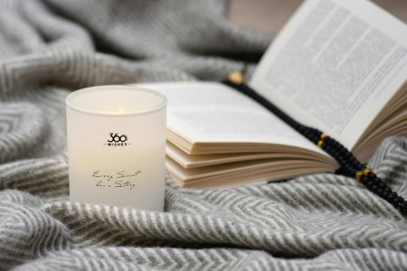 A candle and an open book on a soft gray blanket