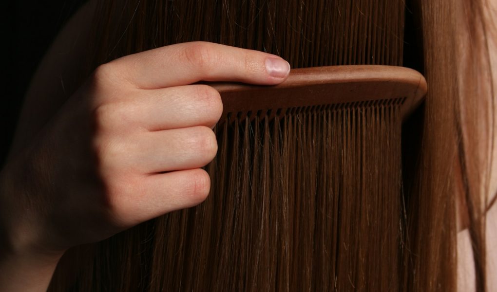 A hand combing long brown hair with a wooden comb