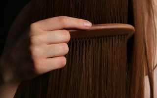 A hand combing long brown hair with a wooden comb