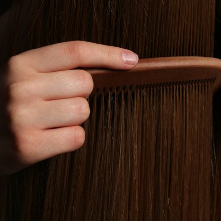 A hand combing long brown hair with a wooden comb