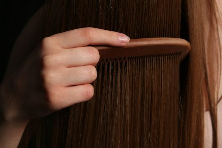 A hand combing long brown hair with a wooden comb