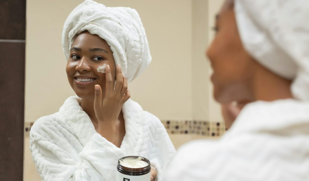 A smiling woman with a towel on her head applying face cream