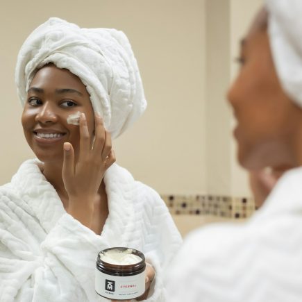 A smiling woman with a towel on her head applying face cream