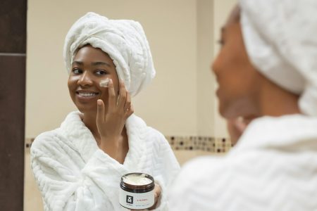 A smiling woman with a towel on her head applying face cream