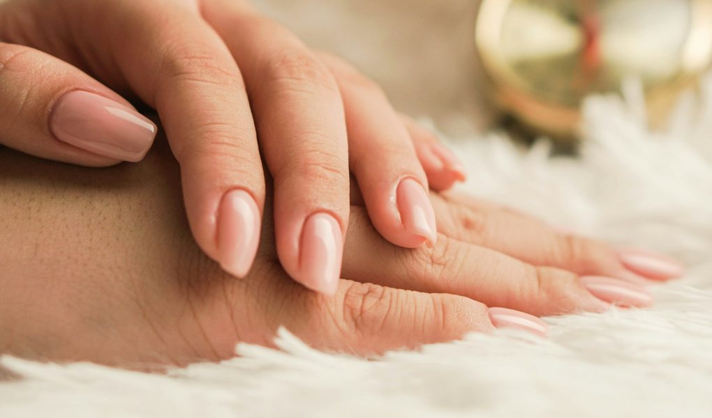 Hands with natural, neatly shaped nails resting on a soft white rug