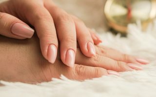Hands with natural, neatly shaped nails resting on a soft white rug