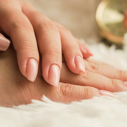 Hands with natural, neatly shaped nails resting on a soft white rug