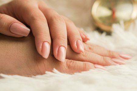 Hands with natural, neatly shaped nails resting on a soft white rug
