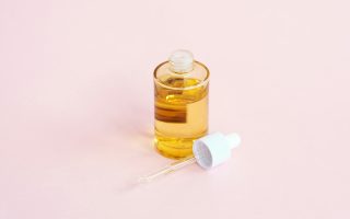 A skincare serum bottle and dropper on a pink surface