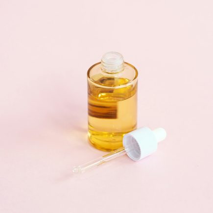 A skincare serum bottle and dropper on a pink surface