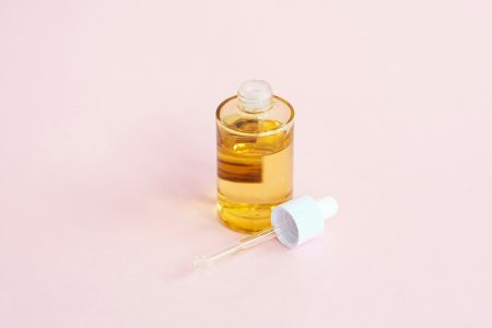 A skincare serum bottle and dropper on a pink surface