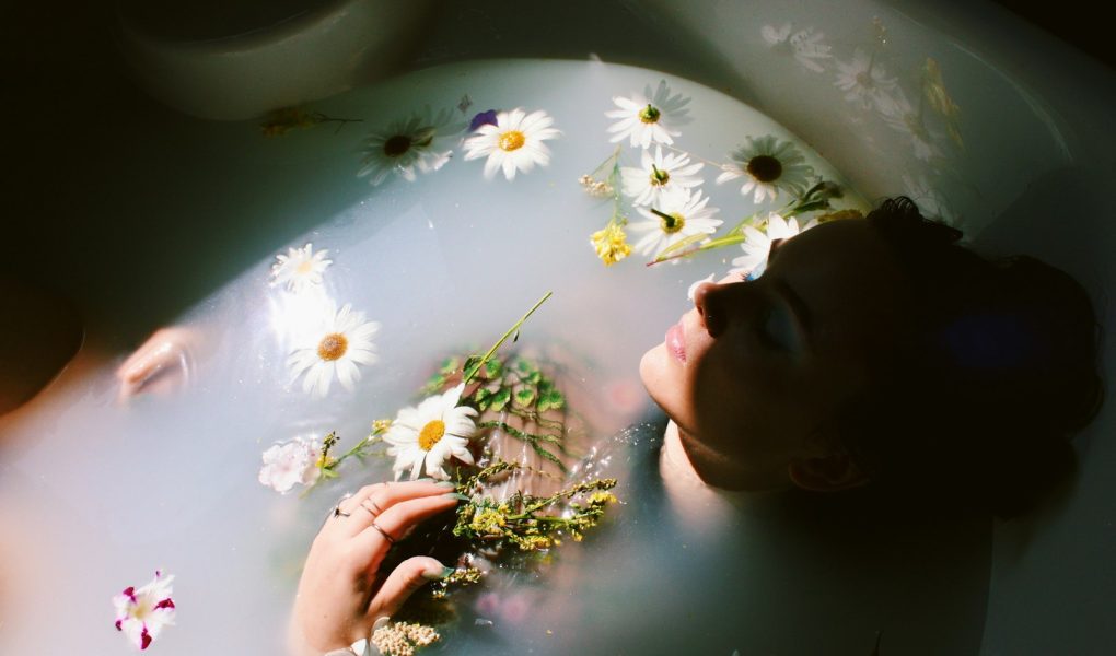 A woman relaxing in a bath with floating daisies