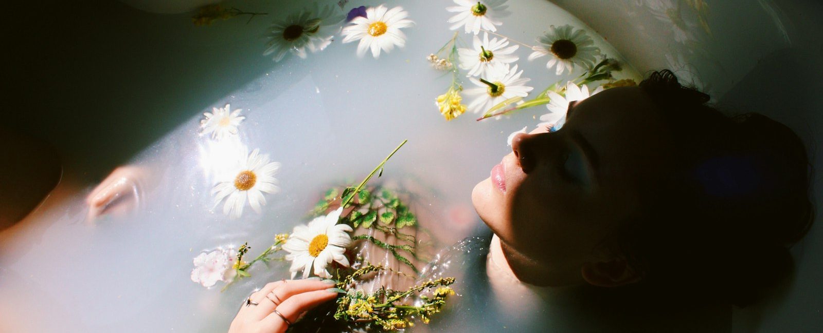 A woman relaxing in a bath with floating daisies